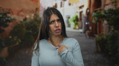 Genç bir kadın gün ışığında dar bir sokakta kendini işaret ediyor; reddedilme..