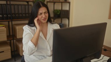Dişi ağrıyan bir kadın iş yerinde masasında oturuyor. Üzüntülü ve endişeli görünüyor. Etrafı dosyalar ve bilgisayarlarla çevrili..