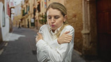 Beyaz gömlekli kadın, eski bir şehir sokağında üşüdüğünü hissediyordu. Ortaçağ açık hava manzarasının ortasında ısınmak için kendini kucaklıyordu..