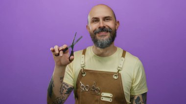 Önlük takan ve elinde makas tutan kel sakallı bir adam canlı mor bir arka plana, dövmeli kollara ve kuaför aletlerine güvenerek gülümsüyor..