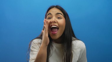 Kadın, Latin kökenli, genç, izole edilmiş mavi arka plan çekimini yaparken elini kaldırıyor..