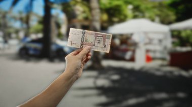 Bir şehir caddesinde, Suudi riyal banknotunun el ele tutuşması, şehir ortamında bir adamın karıştığı mali işlem ya da para değişimi sahnesini resmediyor..