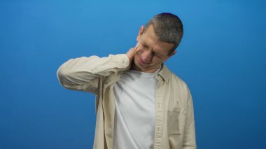 Sıradan giyinmiş bir adam mavi arka planda boynuna dokunuyor. Rahatsızlığını dışa vuruyor, dışlanıyor ve acı dolu bir ifadeyle yukarıya bakıyor. Bu da boyun ağrısının hafifletilmesi gerektiğini gösteriyor..