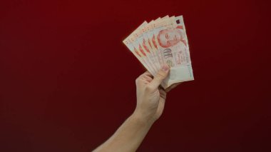 Kırmızı duvar arkaplanına karşı elinde Singapur dolarları tutan adam, izole ortamda para ve finans kavramlarını gösteriyor..
