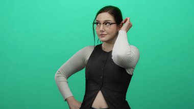 Gözlüklerini parlak yeşil arka plana göre ayarlayan kadın kendine güveni ve tarzı esmer saçlı ve şık giyimli..