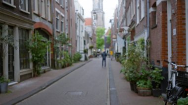 Tuğla binalar ve bulutlu gökyüzü altındaki yemyeşil bitkilerle büyüleyici, dağılmış bir Avrupa caddesinde gezinen adam, tuhaf bir şehir ortamının özünü yakalıyor..