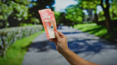 Filipinli banknotların el ele tutulması açık şehir parkında belirgin bir şekilde sergilenmesi finans, yatırım fırsatları ve ekonomik işlemleri yansıtır.