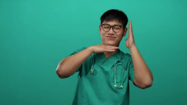 Yeşil önlüklü, steteskoplu genç Çinli adam izole edilmiş yeşil arka plan duvarına gülümsüyor..