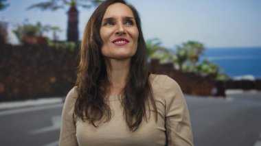 Gülümseyen genç İspanyol kadın, güneşli sahil geçidinde kaya boynuzlarıyla el kaldırıyor..