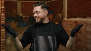 İnşaat alanında gülümseyen önlük ve eldiven takan sakallı genç adam, kapalı servis ya da devam eden bir iş öneriyor..