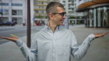 Gözlüklü bir adam şehir caddesinde duruyor. İki elini de parlak çizgili bir tişörtle uzatıyor. Arkaplanda binalar ve kaldırımlarla güvenle gülümsüyor..