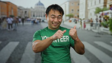 St. Peter Meydanı, Vatikan 'da yeşil tişörtle gülümseyen gönüllü genç adam pozitifliğini ve nişanını ifade ediyor..