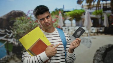 Sahilde sırt çantalı, çizgili tişörtlü, elinde sarı klasörlü, tropikal dekor ve açık hava dekorlarıyla çevrili Kanada pasaportlu adam. Düşünceli bir ifade..