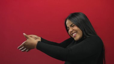 Kadın arkaplana yaslanırken kollarını uzatıyor. Bu arada Latin kökenli genç bir kadın, izole edilmiş kırmızı bir duvarda vücut buluyor..