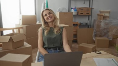 Yeni evdeki kutuları açan kadın dizüstü bilgisayar kullanıyor. Parlak bir oturma odasında malzeme paketliyor. Yerleşirken heyecan ve verimlilik öneriyor..