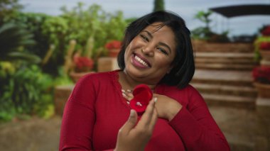 Parktaki kadın neşeyle yüzük kutusunu tutuyor. Açık havada evlenme teklif ediyor. Latince artı boyut mutlu nişanlı kadın..