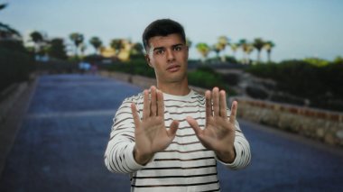 Bir şehir sokağında el kol hareketi yapan genç adam, açık bir şehir ortamında ihtiyatını dile getiriyor..