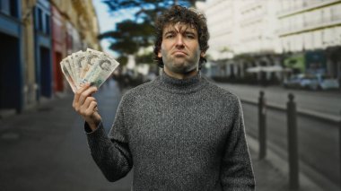 Bir şehir caddesinde elinde İngiliz sterlini olan İspanyol bir adam kendine güvenen bir ifade sunuyor, parayı ve şehir yaşam tarzını ön plana çıkarıyor..