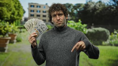 Parkta elinde Amerikan doları olan İspanyol bir adam düşünceli bir ifadeyle finansal kararı veya yatırım fırsatını sembolize ediyor..