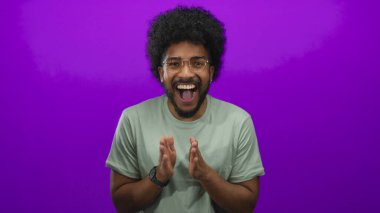 Gözlüklü Afro-Amerikalı adam mutluluk ve enerji gösteren canlı bir mor arka plana gülümsüyor..