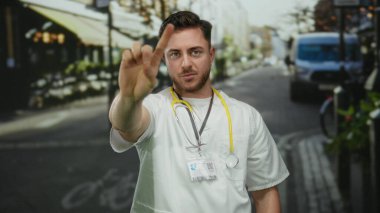 Sakallı ve steteskoplu genç erkek doktor şehir geçmişinde bulanık şehir geçmişine sahip değil, beyaz önlük giyiyor ve açık havada aktif çevrede kararlılık gösteriyor..