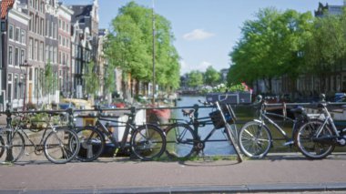 Amsterdam kanalları ön planda odaklı olmayan bisikletler ve arka planda güneşli bir günde klasik Hollanda mimarisi.
