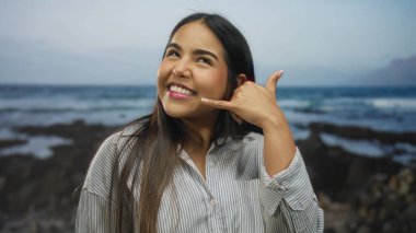 Bir plajda genç Latin asıllı, açık deniz tarzı ve gülümsemesiyle bir kadın el ele tutuşuyor..