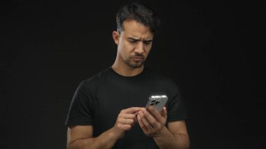 Akıllı telefonlu genç adam izole edilmiş siyah arka planda çeşitli duygular ifade ediyor. Hayal kırıklığı ve zafer gibi..