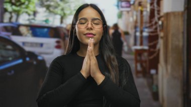 Kalabalık bir sokakta, gözleri kapalı meditasyon yapan bir kadın, sakin bir yüz ifadesi sergiliyor, dinamik bir şehirde dinginliği vurguluyor..