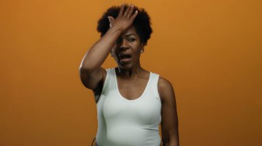 Alnı turuncu arka planda duygularını ifade eden beyaz kolsuz bluz giyen bir kadın çeşitli sözlü olmayan iletişim hareketleri sergiliyor..