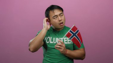 Genç Asyalı adam Norveç bayrağını tutarken pembe arka planda hareketler yapıyor..
