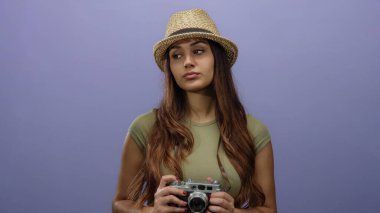 Mor arka planda kamera tutan, şapkalı ve yeşil gömlekli bir kadın. Rahat turist havası var. Genç İspanyol kadınları vurguluyor..