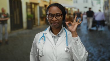 Sokakta steteskopla gülümseyen doktor kadın arka planda bulanık binalarla el hareketi gösteriyor..