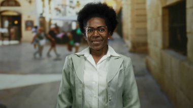 Afro-Amerikalı bir kadın şehir caddesinde açık havada, iş kıyafetleri içinde, hareketli bir şehir ortamında kendine güven ve profesyonellik yayıyor..