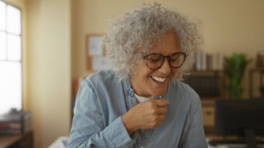 Kitaplıklar ve bitkilerle dolu parlak bir ofis odasında neşeyle gülen bir kadın iş yerinde bir anlık mutluluğu yakalıyor..