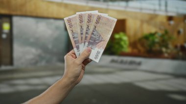 Bir şehir caddesinde İzlanda Krona banknotları tutan bir adam, bulanık arka planlı açık bir şehir ortamında para gösteriyor.