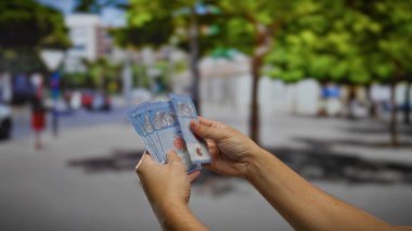 Malezya ringgit paralarını sayan bir adam şehir sokaklarının arka planına karşı, hareketli bir kasaba ortamında finans ve ekonomi kavramlarını vurguluyor..