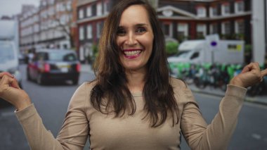 Genç kadın, her iki işaret parmağı da, park halindeki araçlar ve tuğla binalarla dolu işlek şehir caddesinde iki zıt yönü işaret ediyor; kararsızlık tercihi.