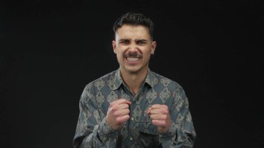 İzole edilmiş siyah arkaplan duvarına karşı duygularını ifade eden genç bir adam değişik ruh hallerinde desenli bir gömlek giyiyor dinamik ifade ve stil aktarıyor.