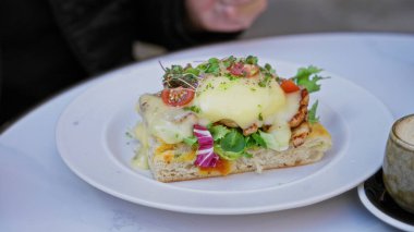 Ellerin gurme yumurtalarını kesiyor. Sıcak bir kafede beyaz bir tabakta taze yeşilliklerle birlikte..