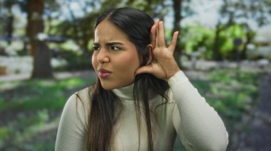 Yeşil bir açık hava parkında dikkatlice dinleyen bir kadın parlak doğal ışık altında tuhaf bir ifade sergiliyor.