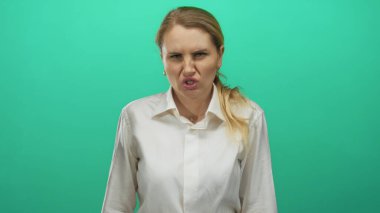 Beyaz gömlekli, yeşil arka planlı, asık suratlı, sarışın, beyaz, genç, yetişkin duygularından hoşlanmayan bir kadın.
