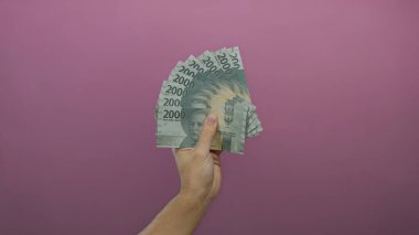Endonezya rupiah banknotlarını pembe bir arka plan üzerinde tutan adam, finans ve zenginlik kavramını resmediyor.