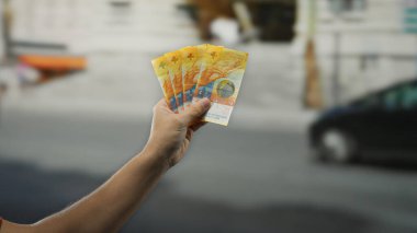 Meşgul bir şehir caddesinde elinde İsviçre frangı banknotları tutan adam, açık hava ortamında finans ve zenginlik kavramını vurguluyor..