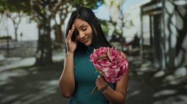 Sokak ortamında pembe çiçekleri tutan bir kadın, coşkulu şehrin ortasında derin bir düşünce ve sükunet duygusu ile genç bir güzellik yayıyor..