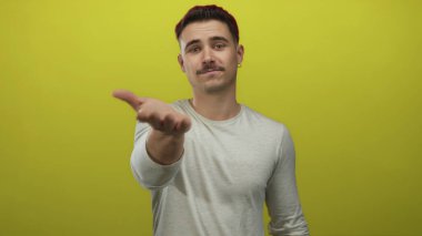 Genç İspanyol asıllı bir adam, canlı sarı arka plana karşı elini uzatıyor. Açık sözlülük ve davetiyeyi dostça bir ifadeyle iletiyor..