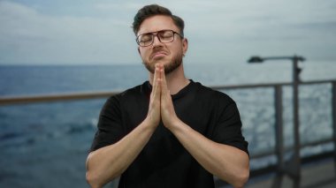 Sakallı genç bir adam açık denizde bir tekne yolculuğunda açık gökyüzünün altında gözleri kapalı bir ruhaniliğe sarılmış, deniz kenarında bir yolcu gemisinde dua ediyor.