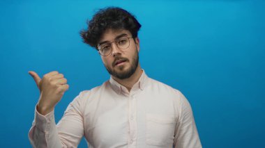 Sakallı ve gözlüklü genç İspanyol bir adam canlı mavi bir arkaplan önünde jestler yapıyor, bir dizi dinamik pozlarla yön, odak ve karar ifadelerini vurguluyor..