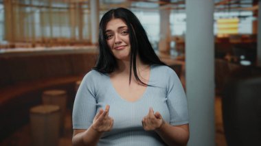 Woman gesturing for money in a restaurant while expressing a pleading gesture, highlighting emotion, curvy figure, casual setting, indoors with soft lighting and modern decor.