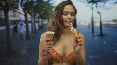 Açık havada güneşli bir sokakta canlı bir bikiniyle dondurma yiyen bir kadın, gençlik coşkusu ve coşkuyla dolu neşeli bir yaz sahnesini vurguluyor..